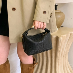 Dettaglio borsa nera in pelle testurizzata con chiusura dorata in un contesto urbano di lusso