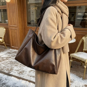 Grand sac cabas marron en similicuir porté sur l'épaule sur un manteau en laine beige