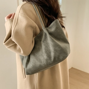 Olive green tote bag shown on shoulder with camel wool coat in minimalist studio