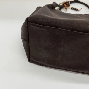 Close-up of dark brown leather tote featuring beaded handle and precise stitching detail