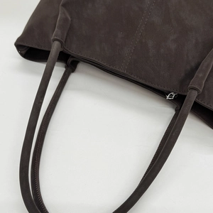 Close-up of dark brown tote bag showing smooth leather texture and top zipper closure