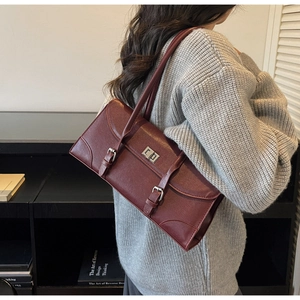 Vue à l'épaule d'un sac sous le bras en cuir bordeaux avec boucles et sangles vintage