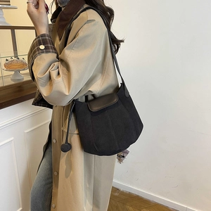 Minimalist black canvas bucket bag with brown leather flap and stylish plush ball charm
