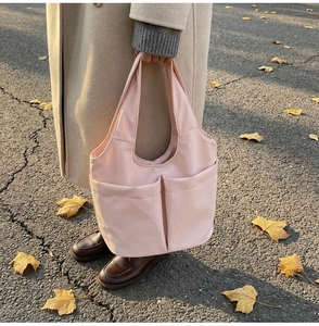 Close-up of light pink nylon tote bag featuring two large functional front pockets outdoors