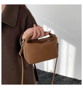 Close-up of caramel leather handbag with gold hardware held by model in wool coat