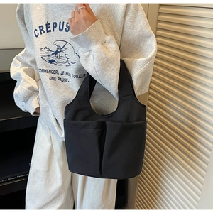Detail of minimalist black tote bag with dual front pockets shown in a lifestyle setting