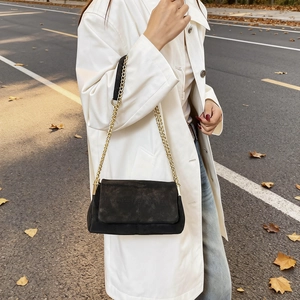 Minimalist black matte shoulder bag with gold chain strap on a stylish autumn street