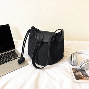 Sac seau minimaliste en daim noir avec bordure en cuir et pompon sur une literie blanche douce