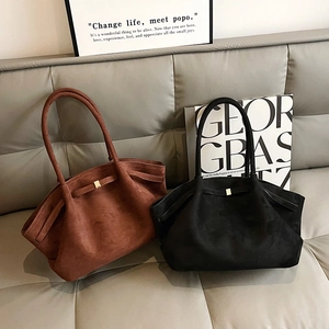 Grands sacs à main en daim marron et noir avec boucles dorées sur un canapé en cuir