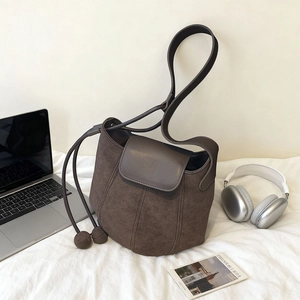 Sac seau minimaliste en daim marron foncé avec finition mate texturée et détails de pompons