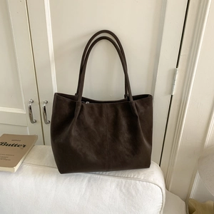 Detailed close-up of dark brown matte leather tote bag with vertical stitching on sofa