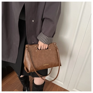 Detail of a vintage brown leather bag featuring cut-out handles and gold stud accents
