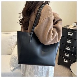 Detailed view of black leather tote bag worn with brown wool coat in a home setting
