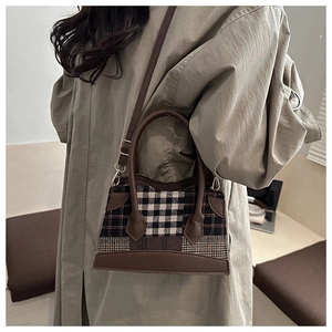 Détail d'un sac à main vintage à carreaux avec garniture en cuir brun porté par un mannequin