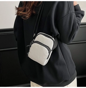 Detail of compact white checkered crossbody bag with double zippers and black nylon strap