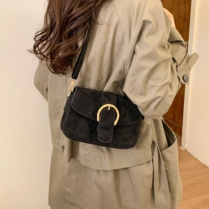 Elegant black matte suede crossbody bag with large gold buckle detail on a trench coat