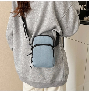 Detail of light blue textured fabric crossbody bag with double zippers and black strap