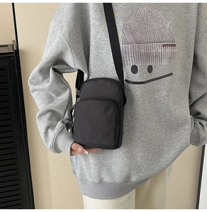 Detail of a black canvas crossbody phone bag featuring dual parallel zipper compartments