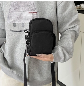 Close-up of a black nylon crossbody bag with dual zipper compartments worn over a grey hoodie