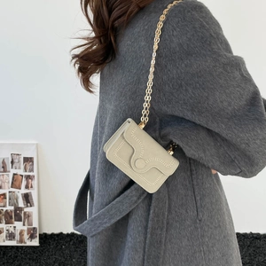 Mini light grey chain crossbody bag with wavy stitching worn with a wool coat