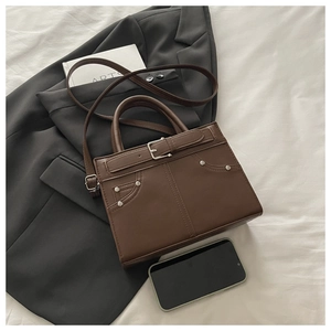 Détail d'un sac cabas marron foncé avec rivets métalliques et sangle sur un décor