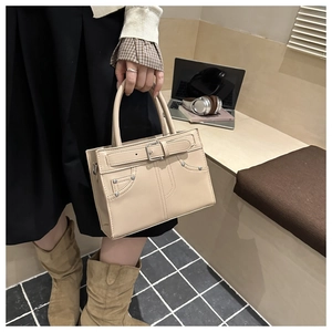 Détail du sac cabas beige avec sangle à boucle et rivets dans un décor de bureau