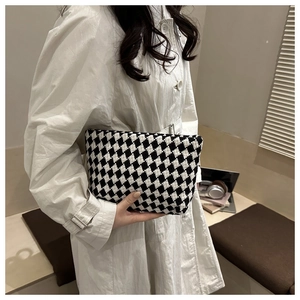 Detail of checkered knit clutch bag held by a model in a minimalist urban setting