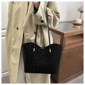 Close-up of black leopard print tote bag with gold hardware worn on a beige trench coat