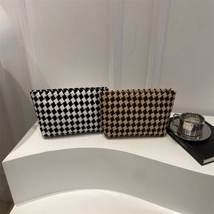 Fashionable checkered woven clutch bags in black and beige on a minimalist white stand