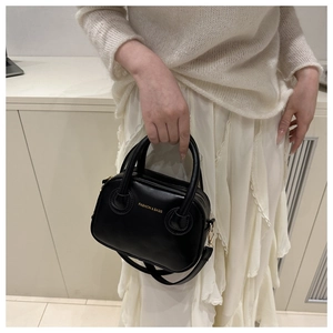 Vista detallada del mini bolso negro con letras doradas y correa de hombro ajustable