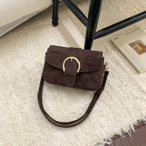 Detail of deep brown suede handbag with large gold ring buckle on plush carpet