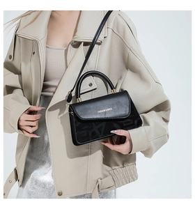 Détail d'un sac bandoulière noir avec lettrage doré et texture grainée du cuir