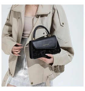Détail du sac bandoulière noir avec texte doré et poignée ronde sur mannequin mode