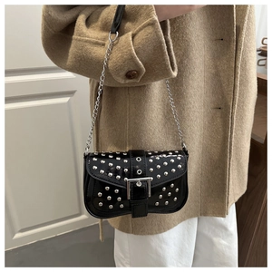 Detail einer schwarzen Lackleder-Schultertasche mit silbernen Nieten und Kette am Model