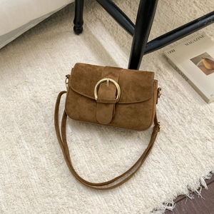 Brown suede shoulder bag with gold metal buckle decoration on white textured rug