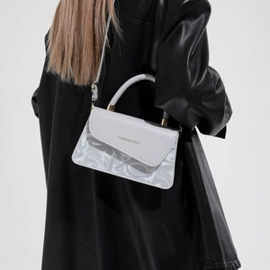 Sac à main gris en cuir avec rabat et détails dorés porté avec un manteau en cuir noir