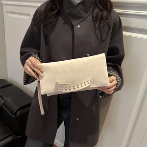 Pochette beige minimaliste en daim avec rivets dorés et dragonne sur un manteau gris