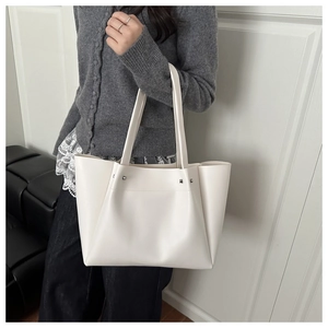 Detail of a creamy white leather tote bag with silver rivet studs and a long shoulder strap