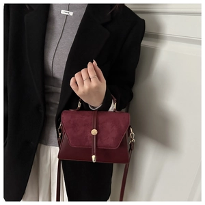 Detail of burgundy crossbody bag featuring matte suede flap and gold cylindrical lock