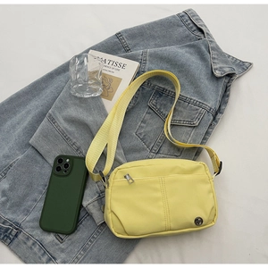 Détail d'un sac bandoulière en nylon jaune clair avec poche zippée et sangle réglable