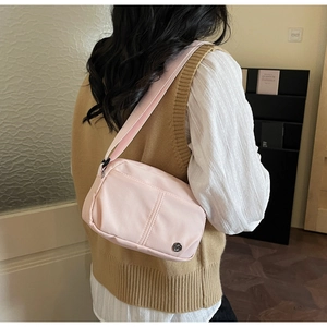 Detail of light pink nylon crossbody bag showing the branded metal logo and fabric strap