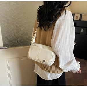 Détail d'un sac bandoulière crème avec logo en métal et bandoulière tissée porté