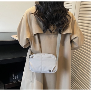 Back view of a light gray nylon crossbody bag with adjustable strap and metal logo