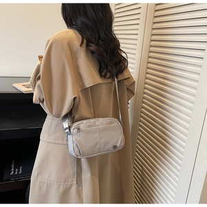 Sac bandoulière en nylon gris clair avec sangle ajustable porté sur un trench-coat kaki