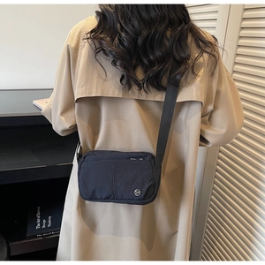 Detail of black nylon crossbody bag with silver metal logo worn on beige trench coat