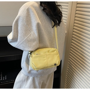 Vue détaillée du sac bandoulière jaune avec fermeture éclair et logo métallique