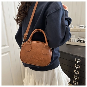 Brown retro leather shell handbag with embossed lettering worn by a model in a home setting