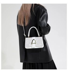 Detail of white leather bag featuring a gold D-ring buckle and textured letter patterns