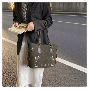 Close-up of cute green suede tote bag with cat face design and brown leather strap