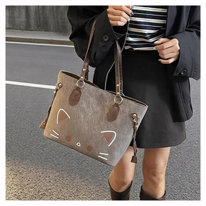 Detail of cute cat motif on grey matte tote bag with brown leather handles and gold rings